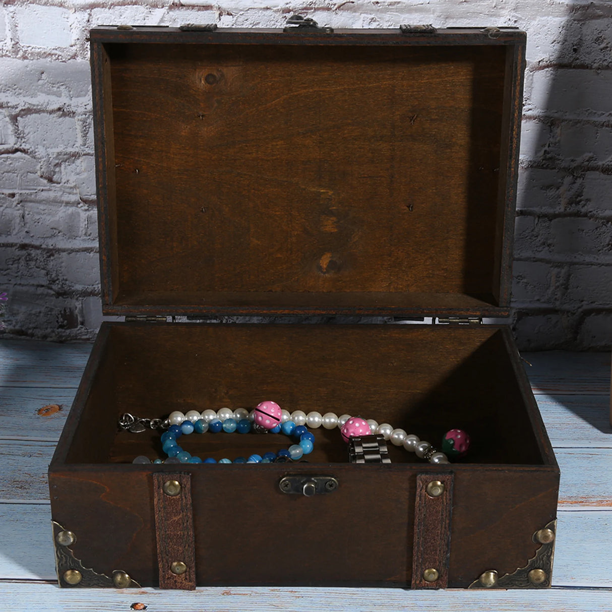 Open wooden jewelry box with jewelry inside against a brick wall background