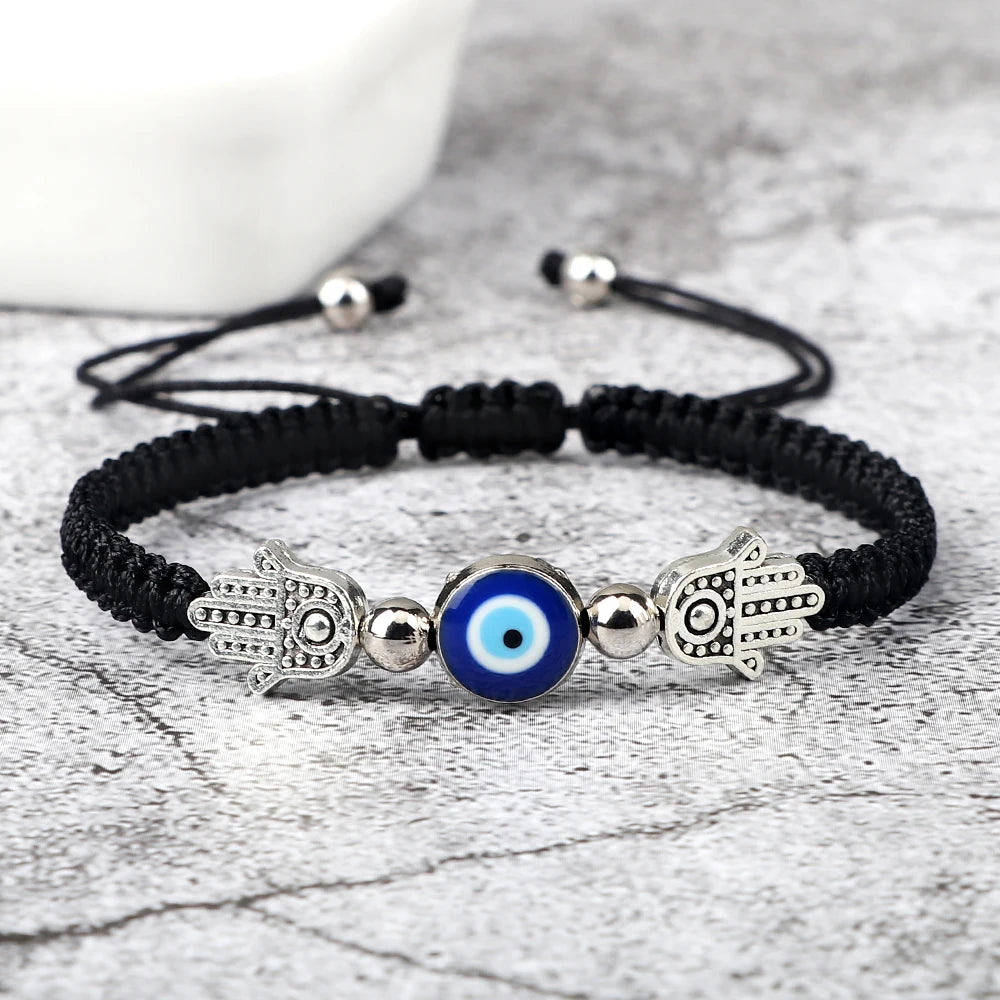 Black braided bracelet with Hamsa hand and blue evil eye charm on a light gray background