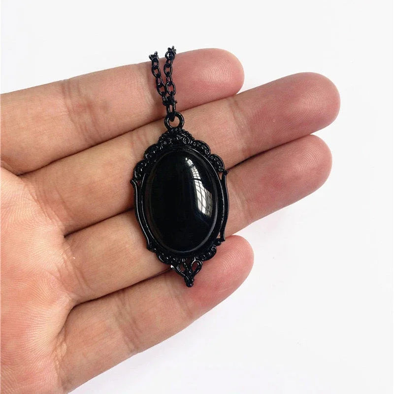 Black pendant necklace held in a hand against a white background