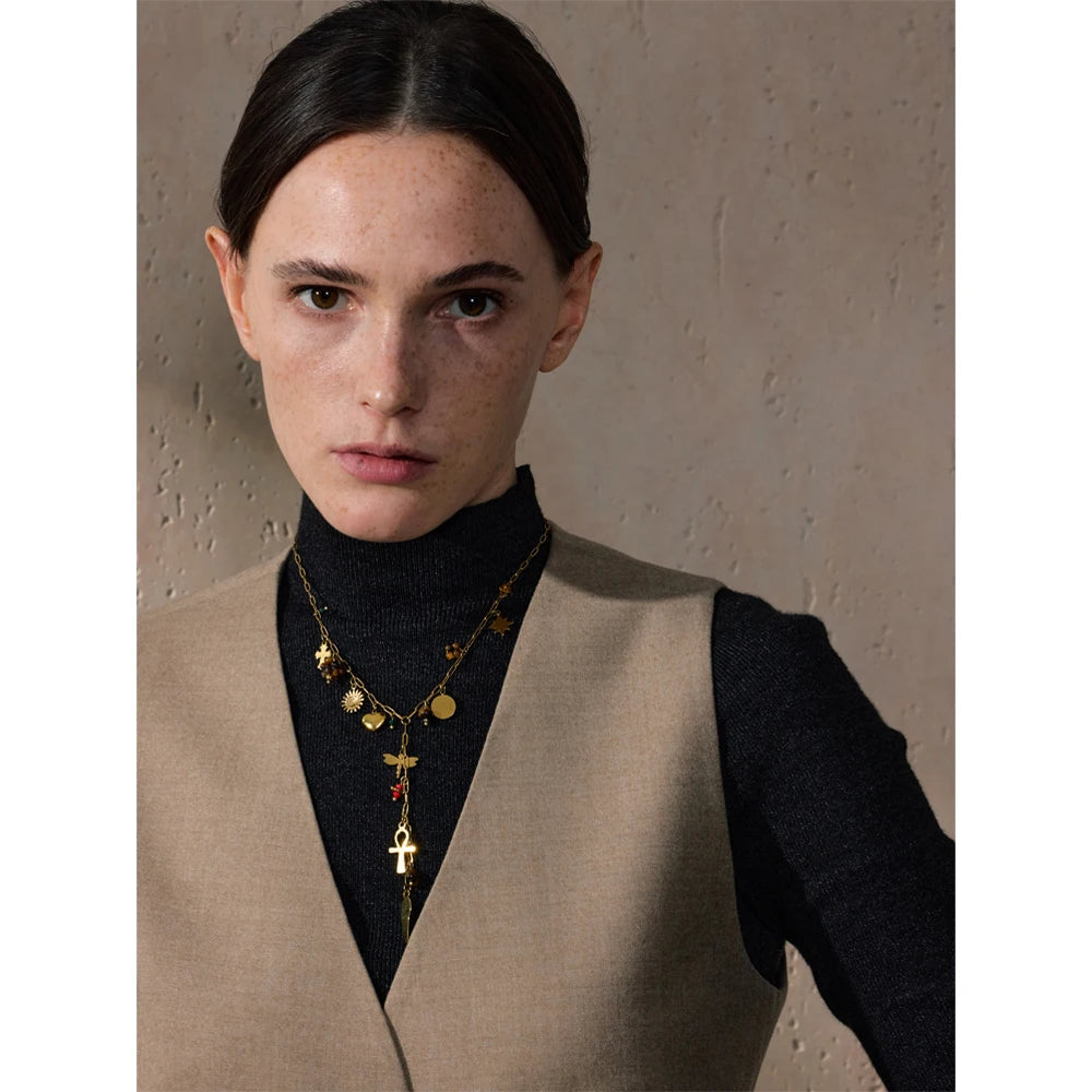 Woman wearing a beige vest over a black turtleneck with a gold necklace against a neutral background