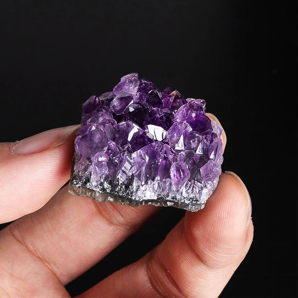 Hand holding a purple amethyst crystal against a black background