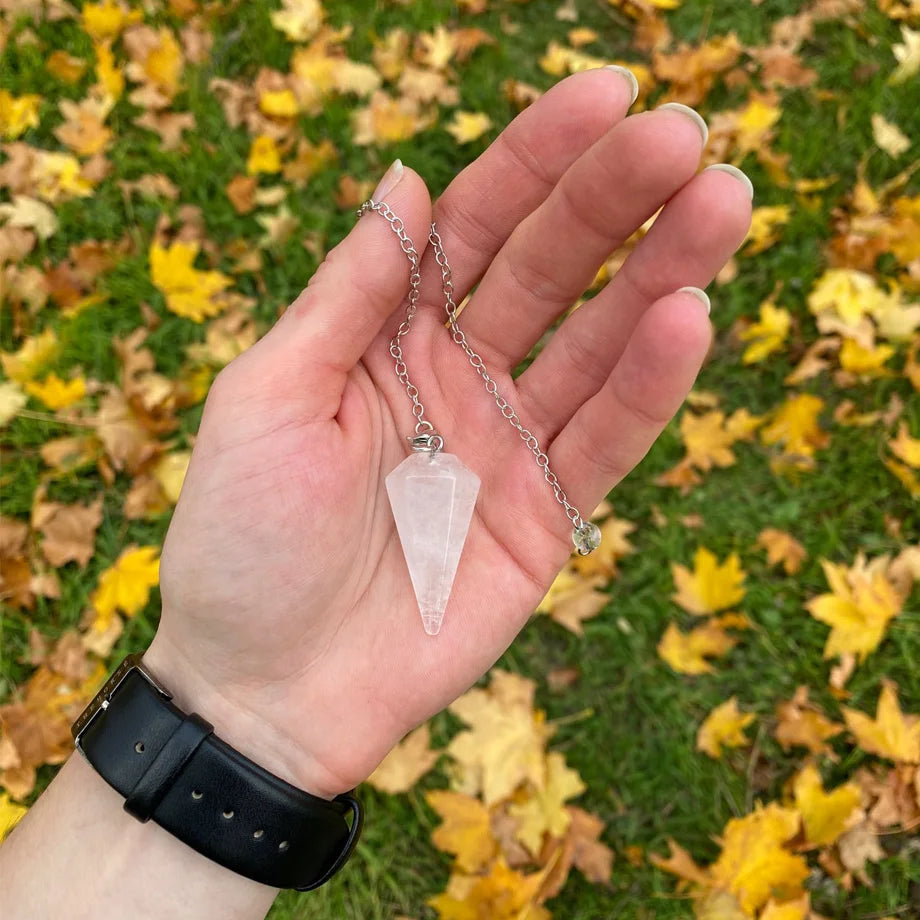 Hand holding a crystal pendulum against a background of autumn leaves