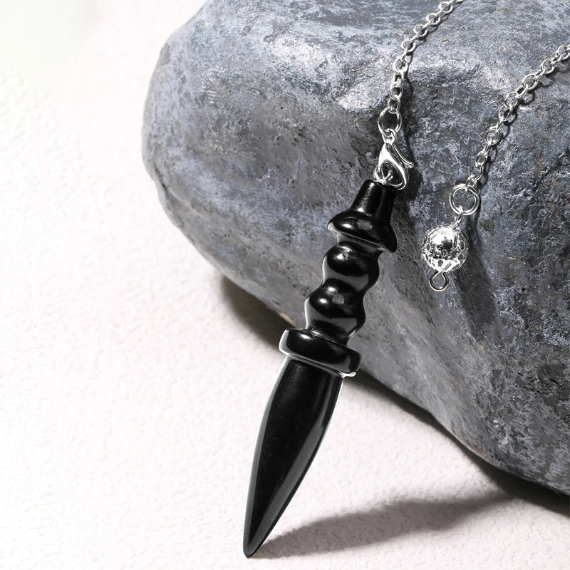 Black dagger-shaped pendant on a chain against a stone background