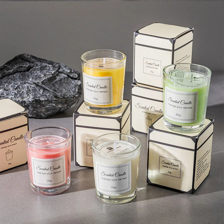 Five scented candles in glass jars with decorative boxes on a gray surface.