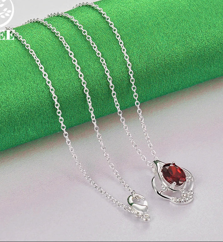 Silver necklace with a red gemstone pendant on a green fabric background