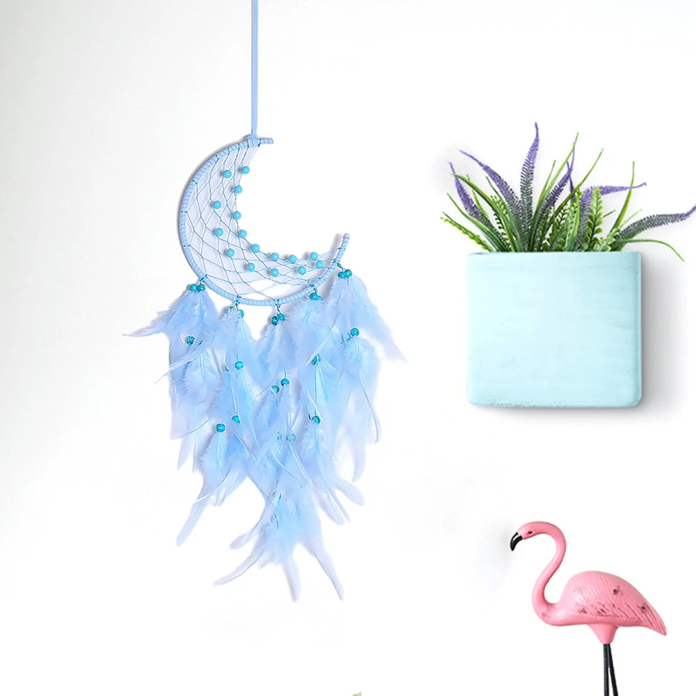 Decorative moon-shaped dreamcatcher with feathers, a small plant in a blue pot, and a pink flamingo figurine on a white background.