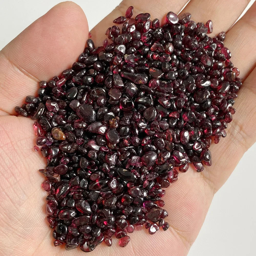 Hand holding a pile of dark red gemstones against a neutral background