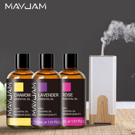 Three bottles of Mayjam essential oils with a diffuser on a wooden surface.