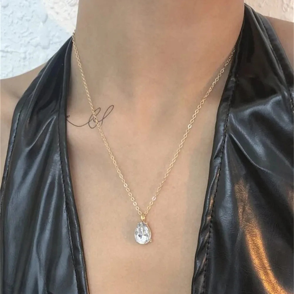 Gold necklace with a pendant worn by a person in a black leather outfit.