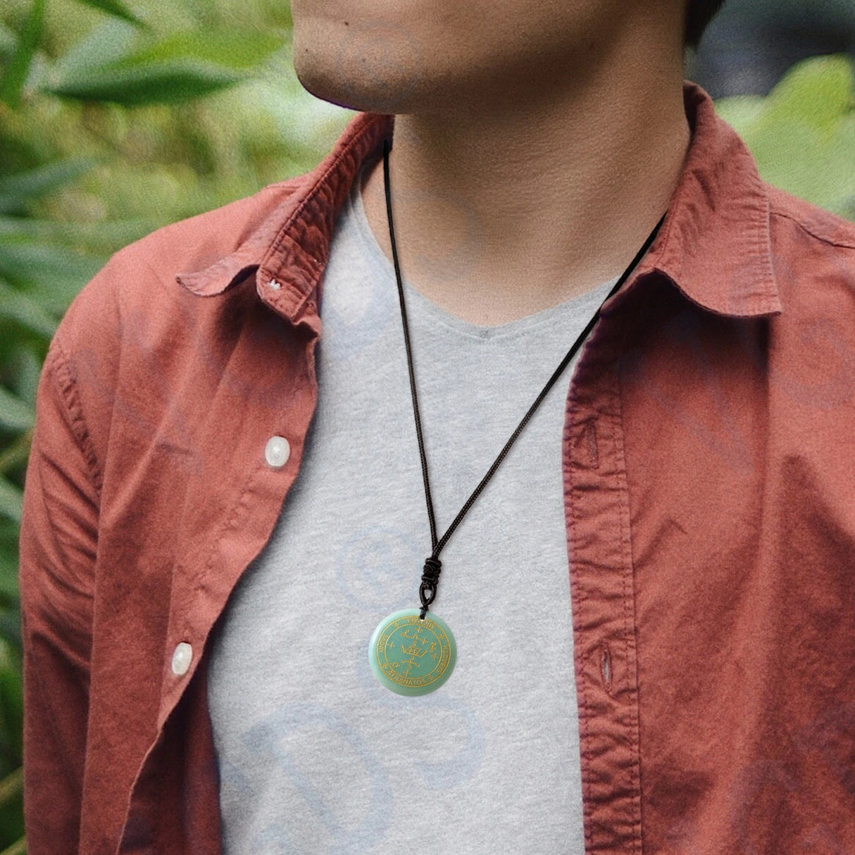 Person wearing a necklace with a green pendant against a blurred natural background