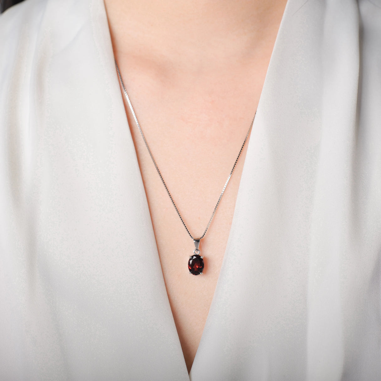 Necklace with a red gemstone pendant worn by a person in a white outfit.