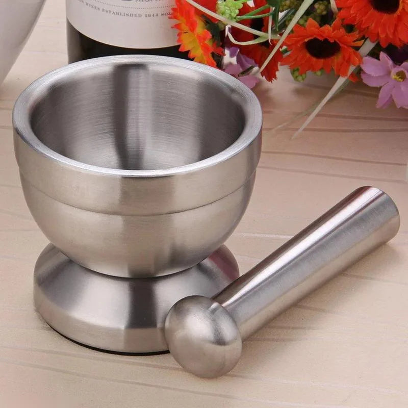 Stainless steel mortar and pestle on a wooden surface with flowers in the background
