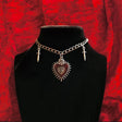 Necklace with heart-shaped pendant and cross charms on a black stand against a red textured background