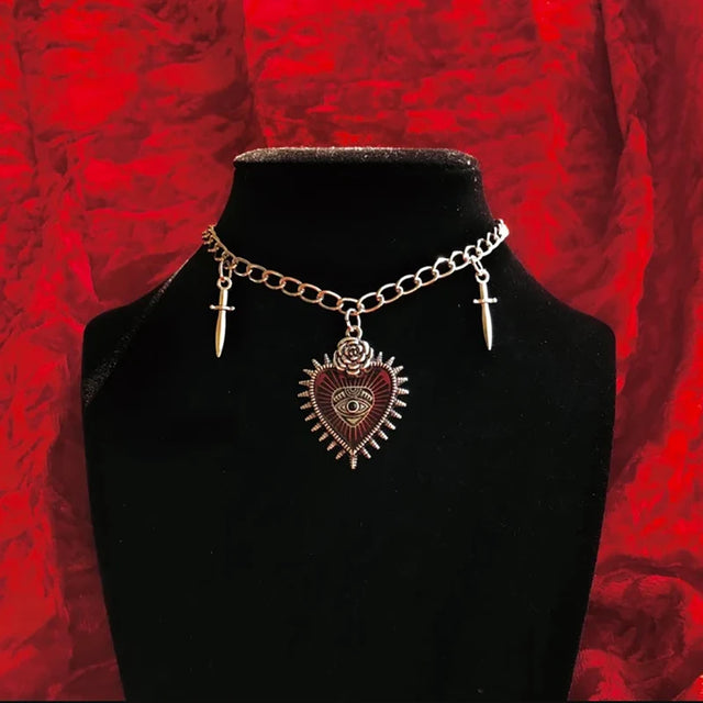 Necklace with heart-shaped pendant and cross charms on a black stand against a red textured background