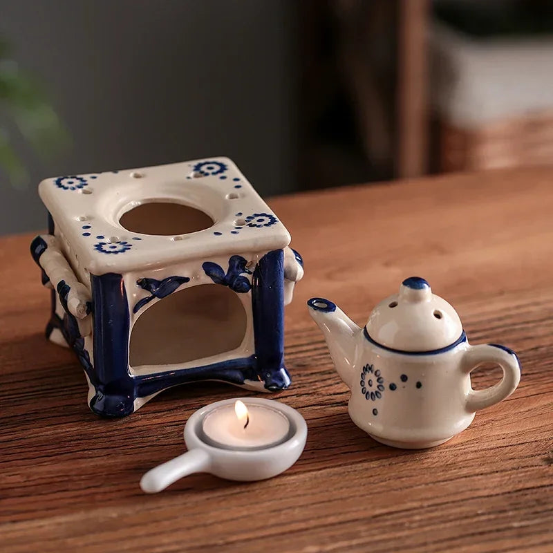 Ceramic tea light holder with a teapot and candle on a wooden surface