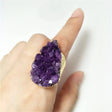 Hand wearing a large purple crystal ring on a white background