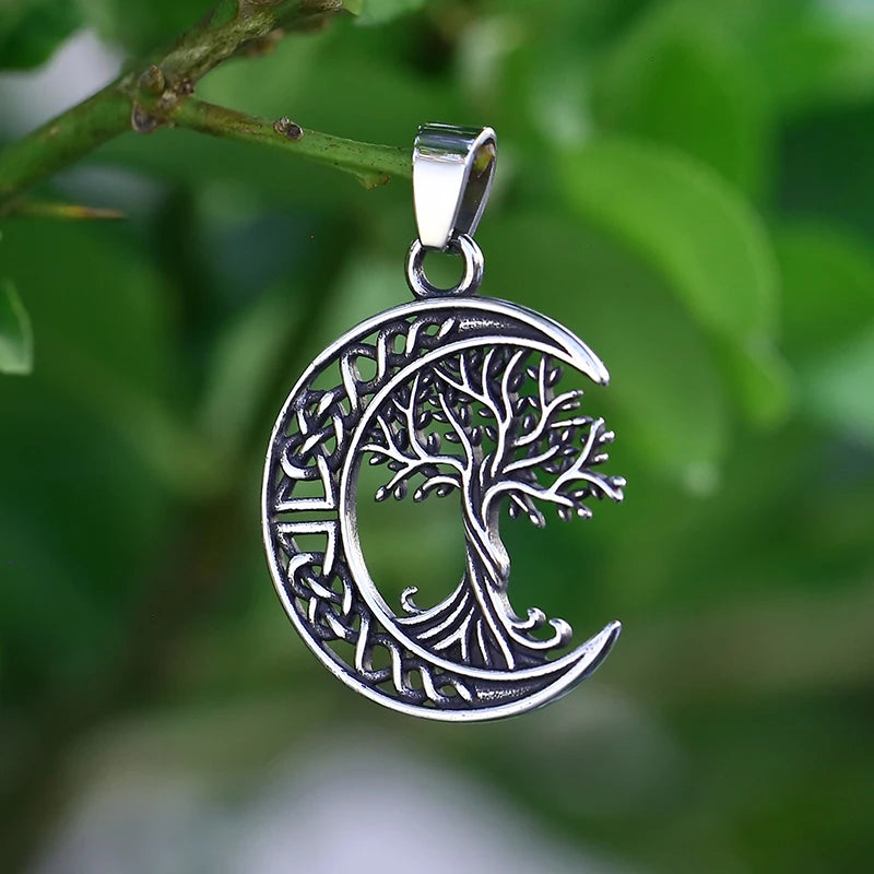 Silver pendant with tree design inside a crescent moon against a green leafy background