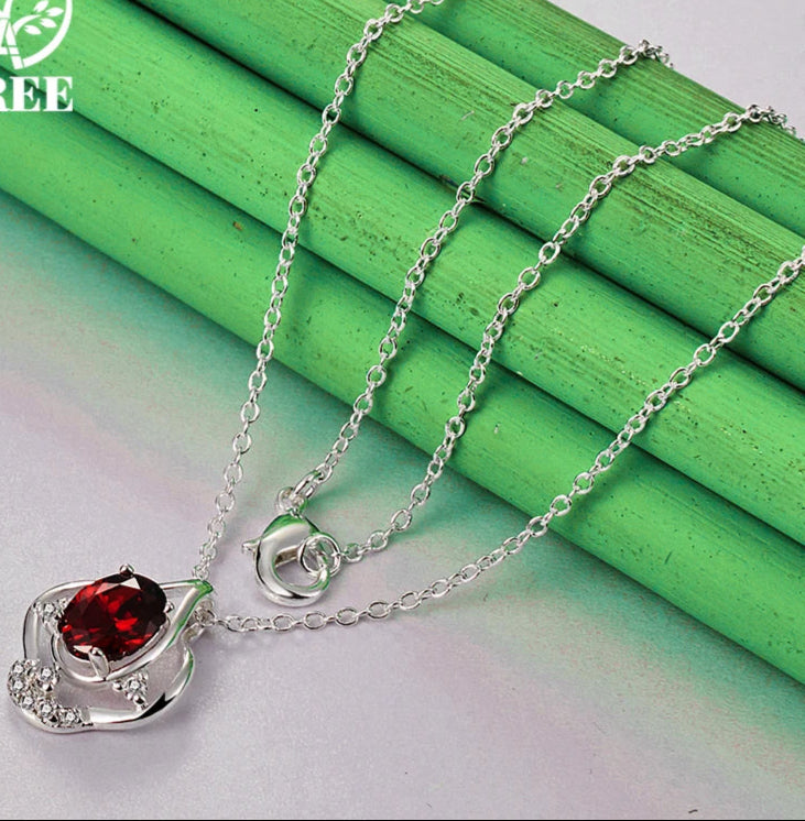 Silver necklace with a red gemstone pendant on a green wooden surface