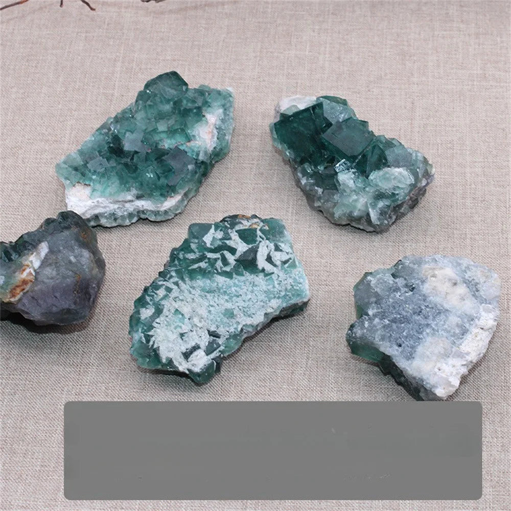 Five green and white crystal rock specimens on a textured beige fabric background