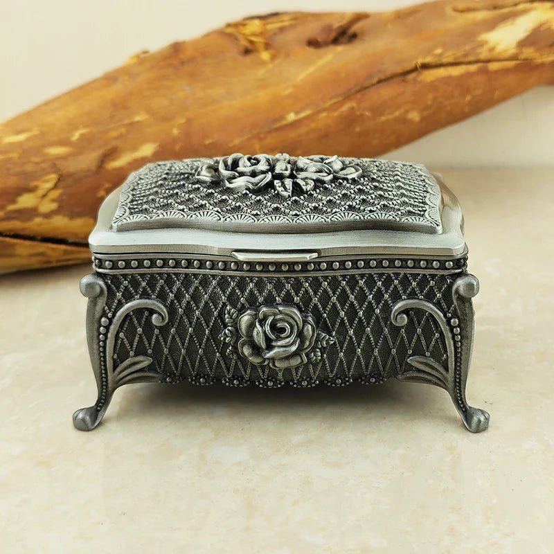 Decorative silver jewelry box with floral designs on a beige surface