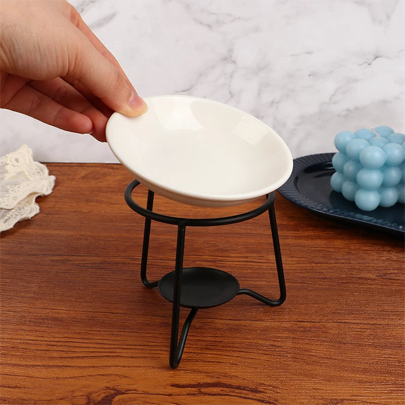 Hand holding a white dish over a black metal stand on a wooden surface.