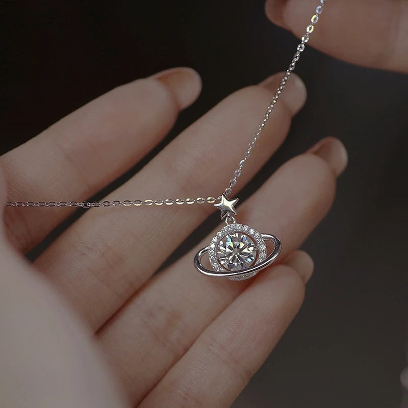 Silver necklace with a planet and star pendant held by a hand against a dark background