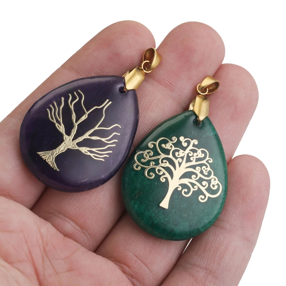 Two teardrop-shaped pendants with gold tree designs on a hand against a white background