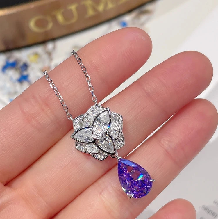 Necklace with a floral pendant and purple teardrop pendant held on a hand, with 'CUMEE' branding.