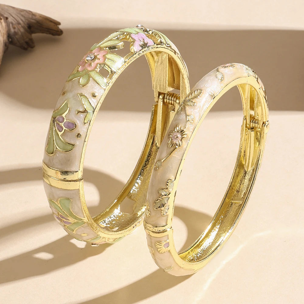 Two gold bangles with floral designs on a beige background