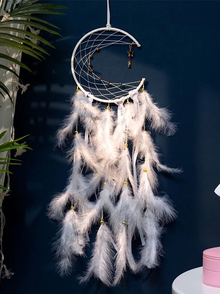 White dreamcatcher with feathers hanging against a dark blue wall.