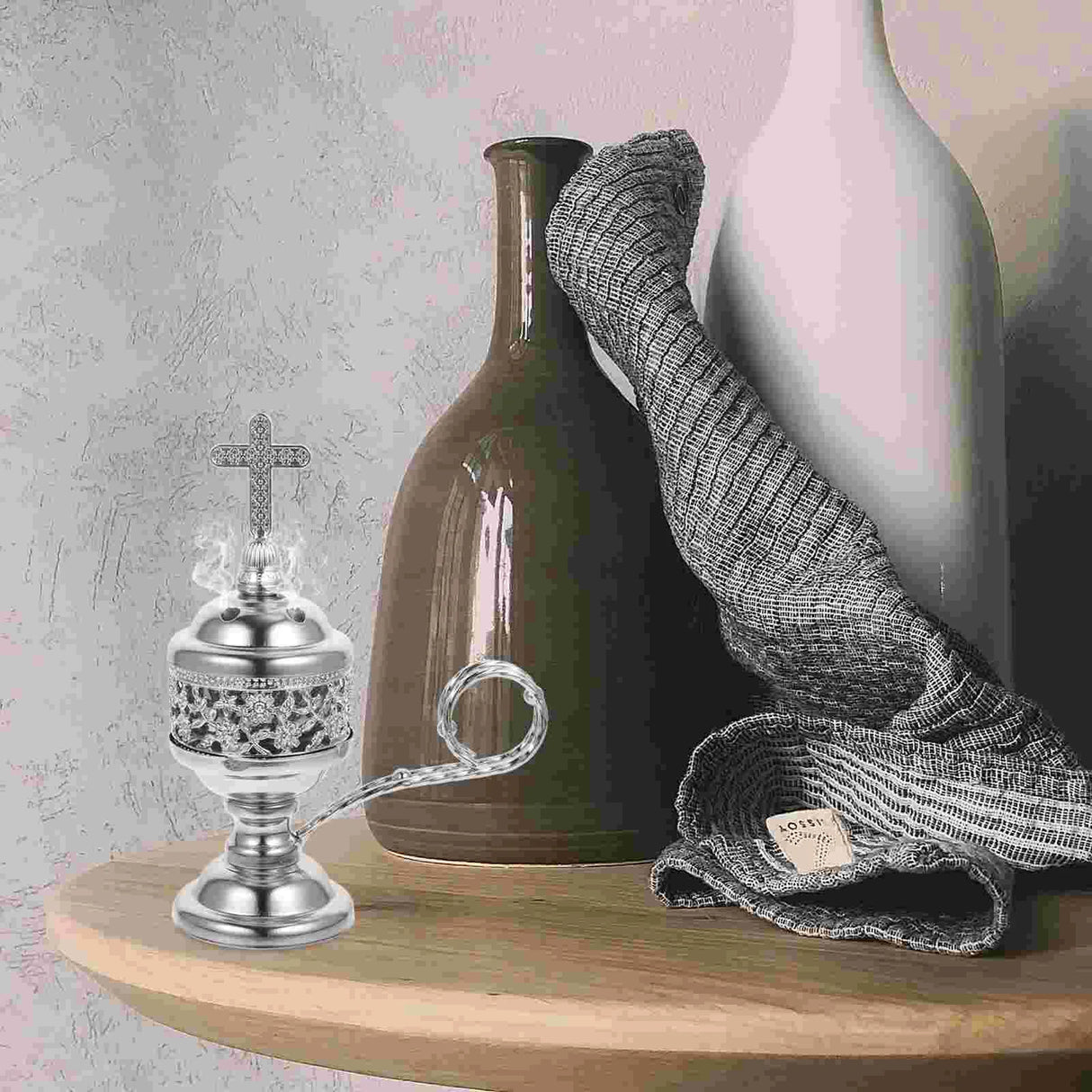 Decorative items including a silver censer, green vase, pink vase, and gray scarf on a wooden surface.