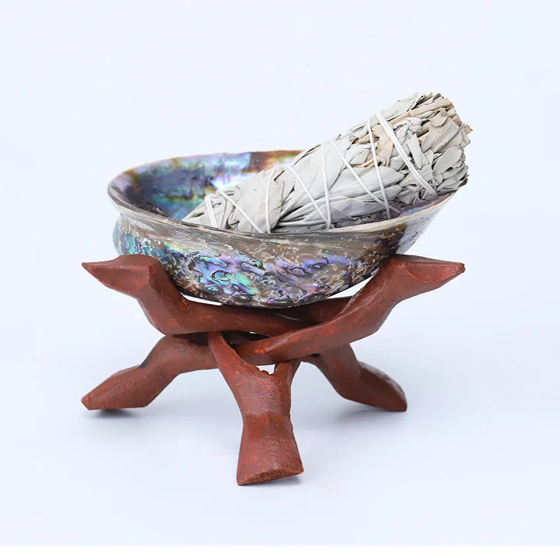 Ceramic bowl with abalone shell design containing sage on a wooden stand against a white background