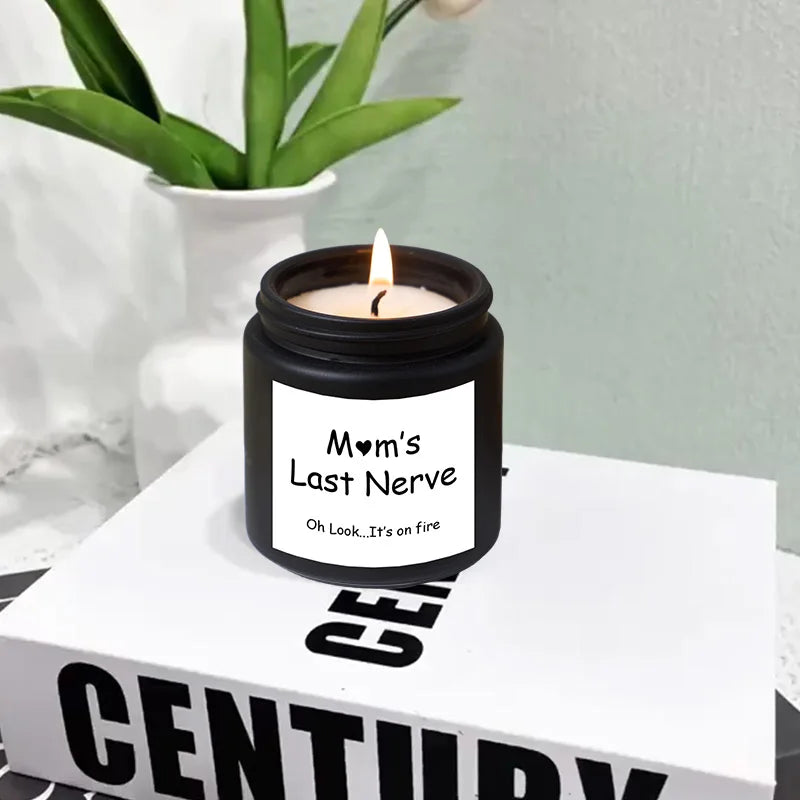 Candle in a black container labeled 'Mom's Last Nerve' on a book with a plant in the background