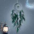 Dreamcatcher with green feathers against a starry night sky