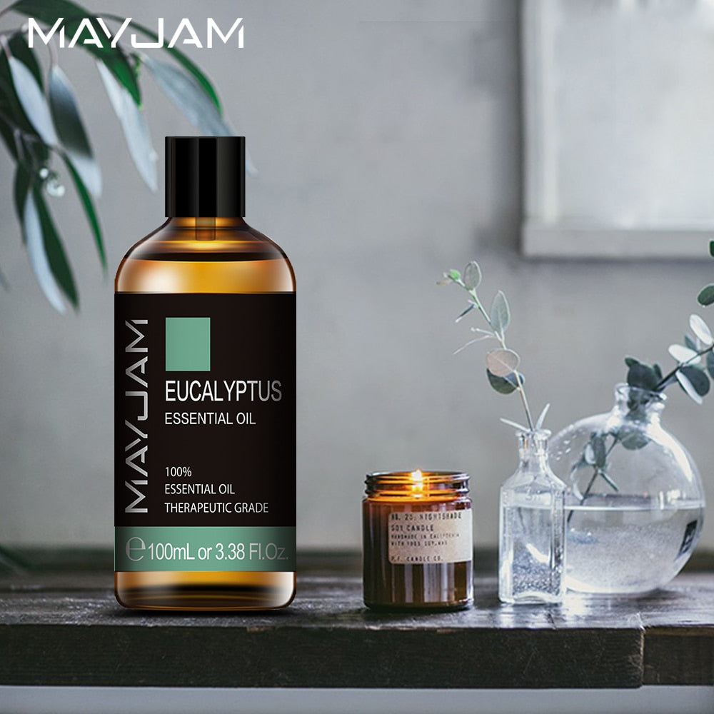 MAYJAM eucalyptus essential oil bottle on a table with a candle and vase in the background.