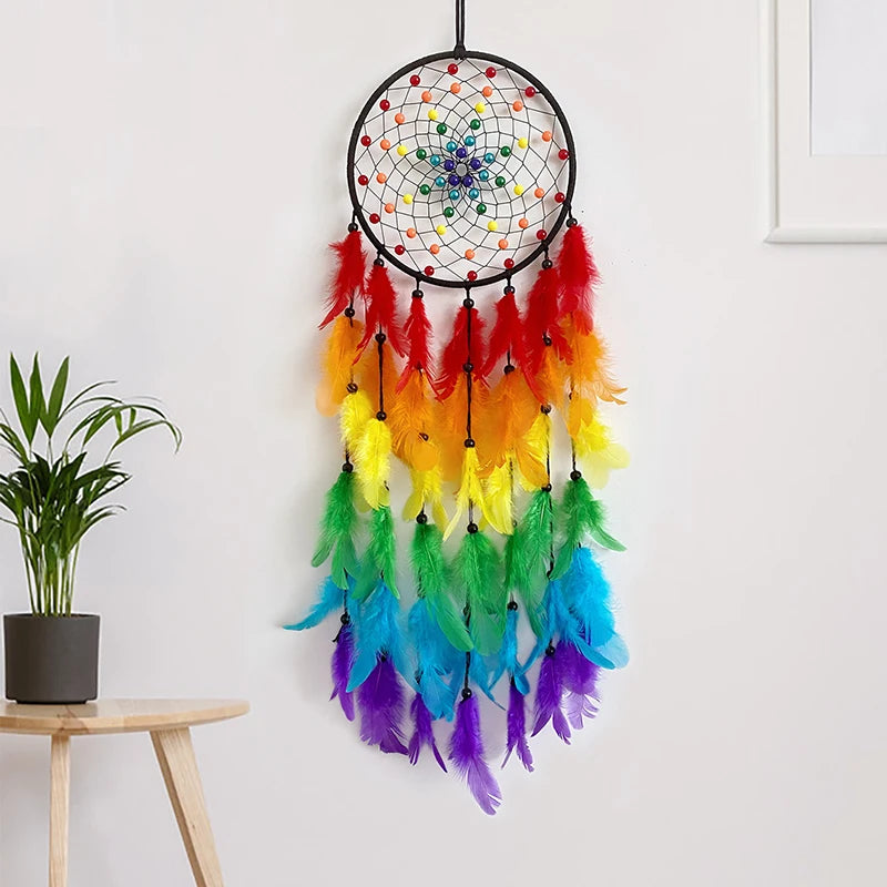 Rainbow-colored dreamcatcher hanging on a white wall with a plant on a table below.