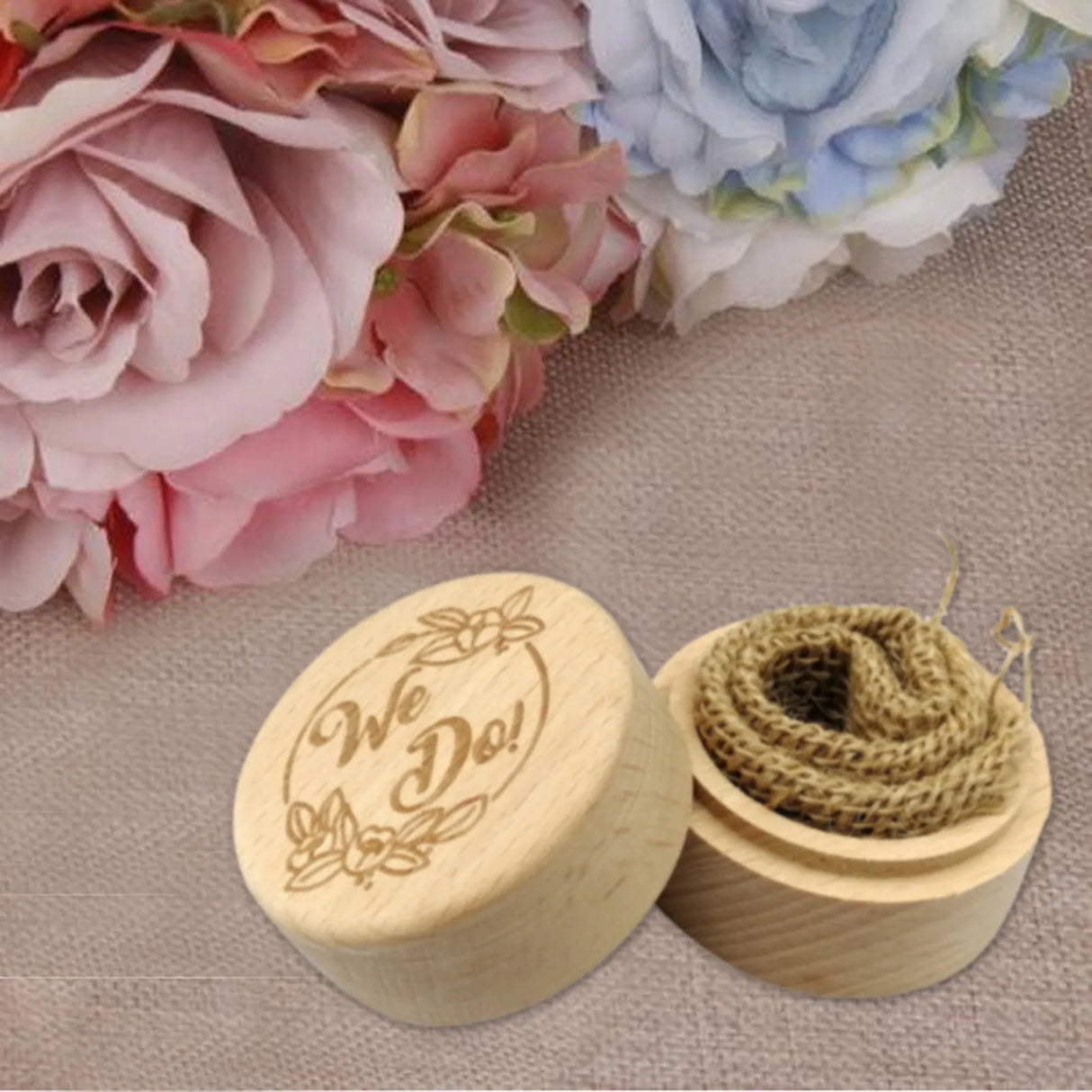 Wooden box with 'We Do!' engraving and a roll of twine, surrounded by flowers on a textured surface.