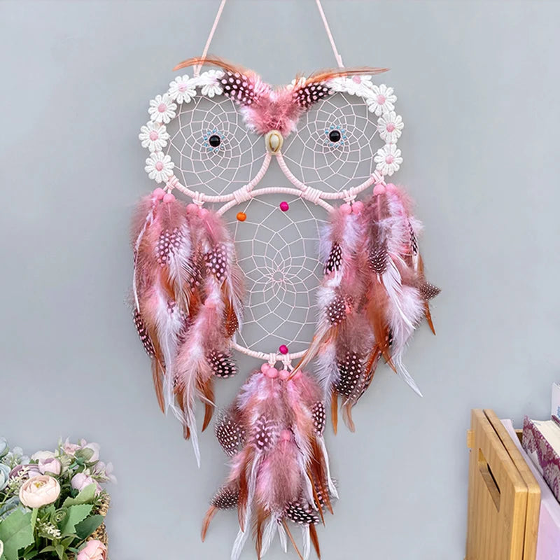 Decorative owl-shaped dreamcatcher with feathers on a light gray wall.