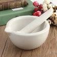 White ceramic mortar and pestle on a wooden surface with flowers and books in the background