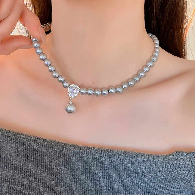 Pearl necklace with a heart-shaped pendant on a model wearing a gray top.