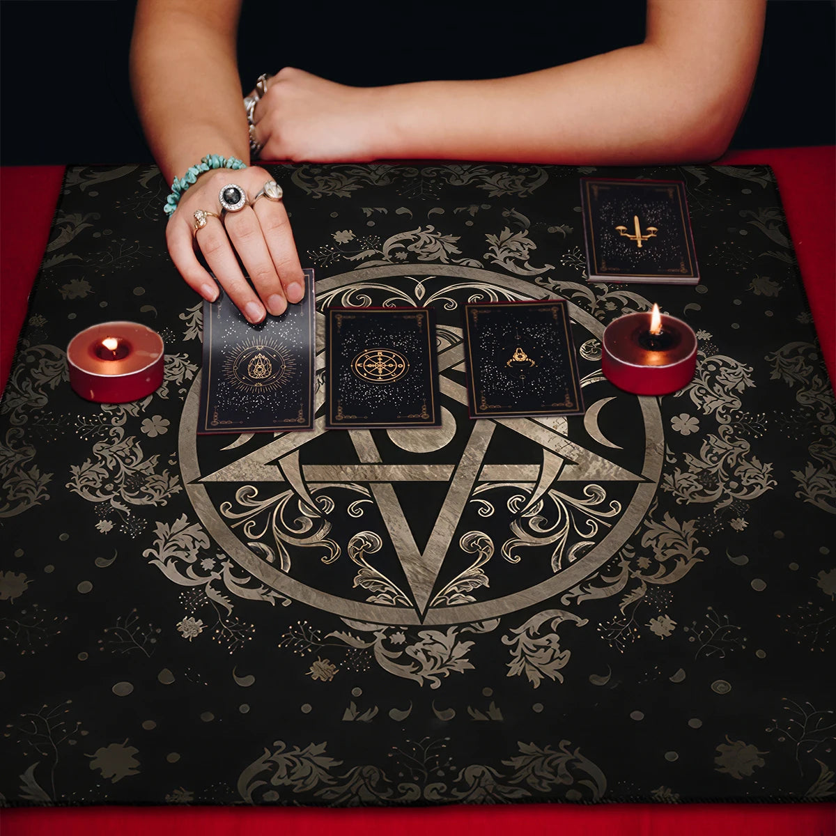 Person holding tarot cards on a black cloth with a pentagram design, surrounded by candles.