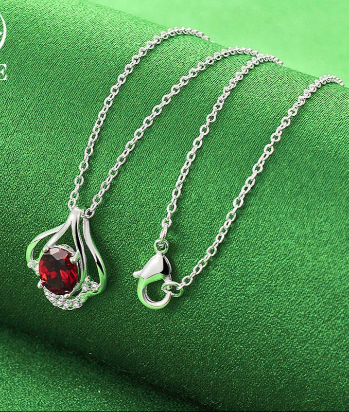 Silver necklace with a red gemstone pendant on a green fabric background