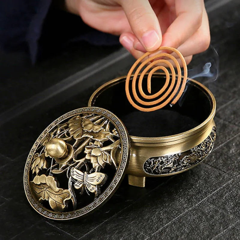 Bronze incense holder with intricate designs on a dark surface, featuring a hand placing an incense coil.