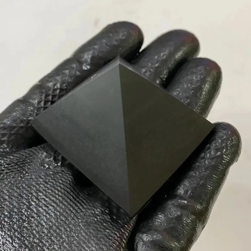 Black pyramid-shaped object held in a gloved hand against a neutral background