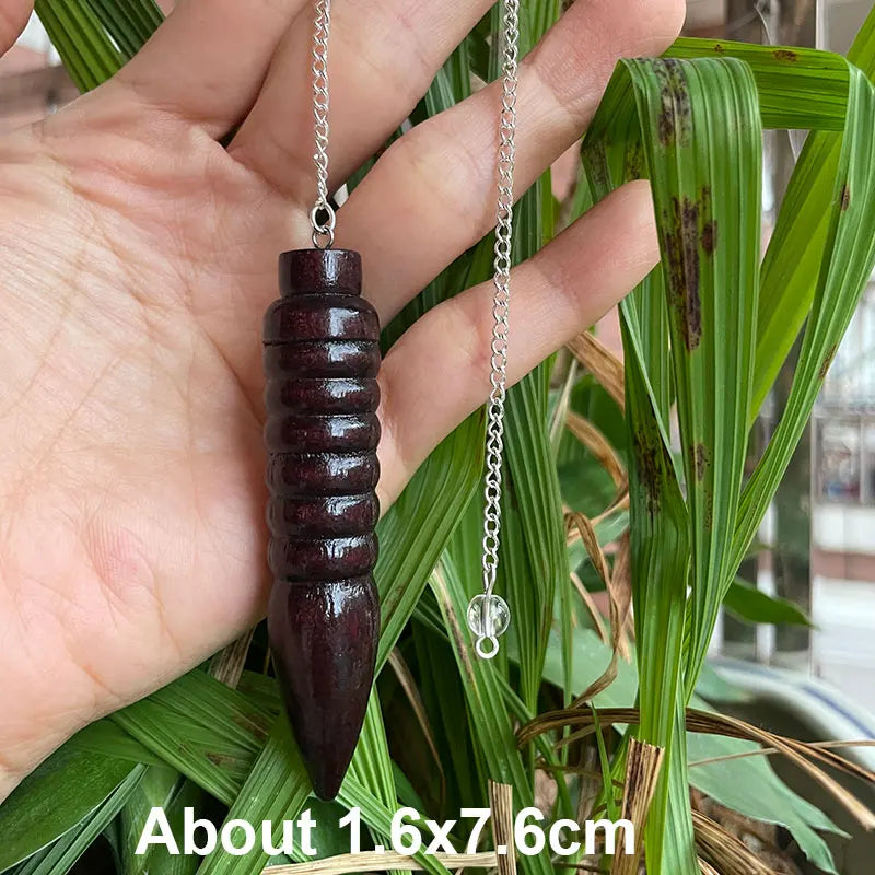 Hand holding a wooden pendant with a silver chain against a green leafy background