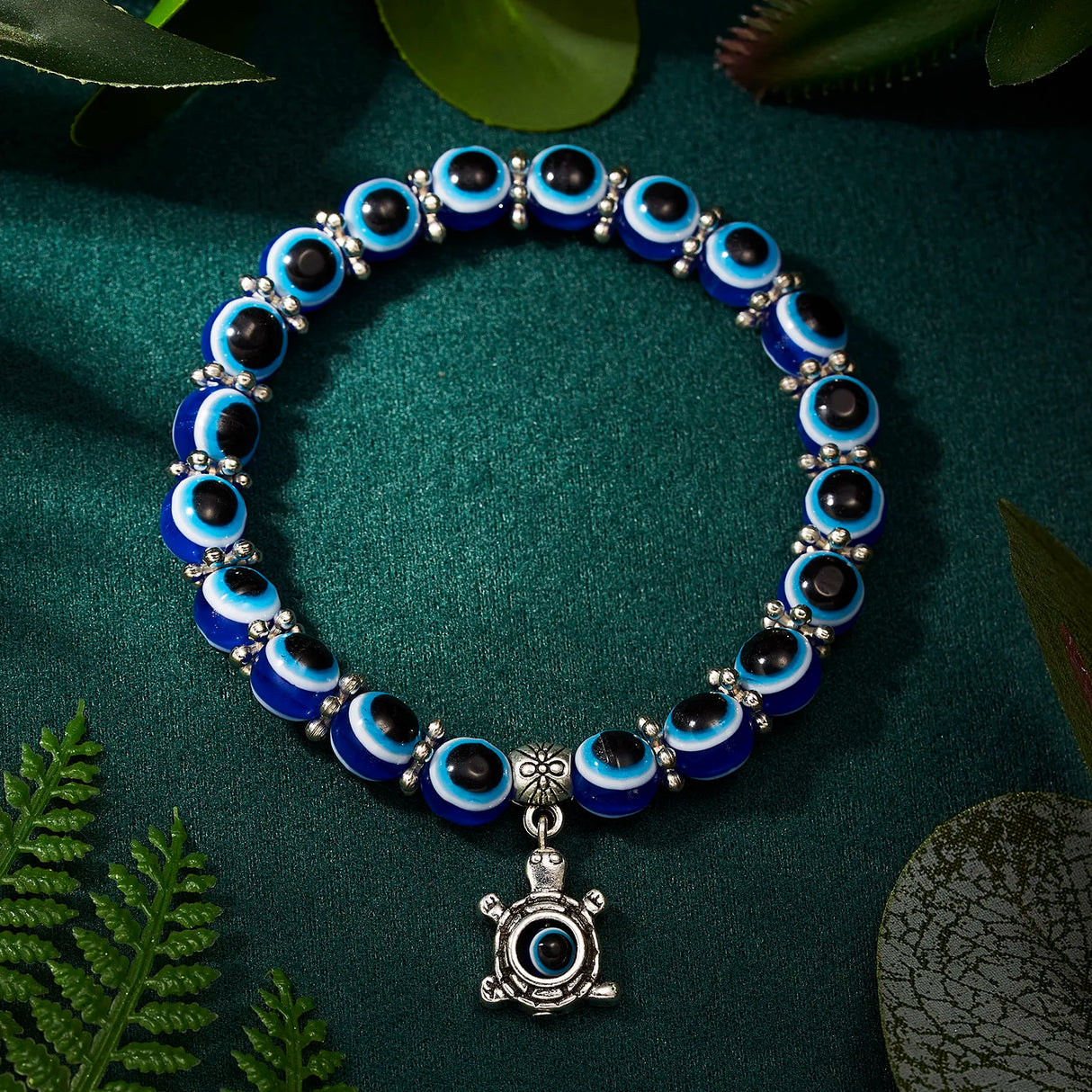 Blue and black beaded bracelet with a silver turtle charm on a green background