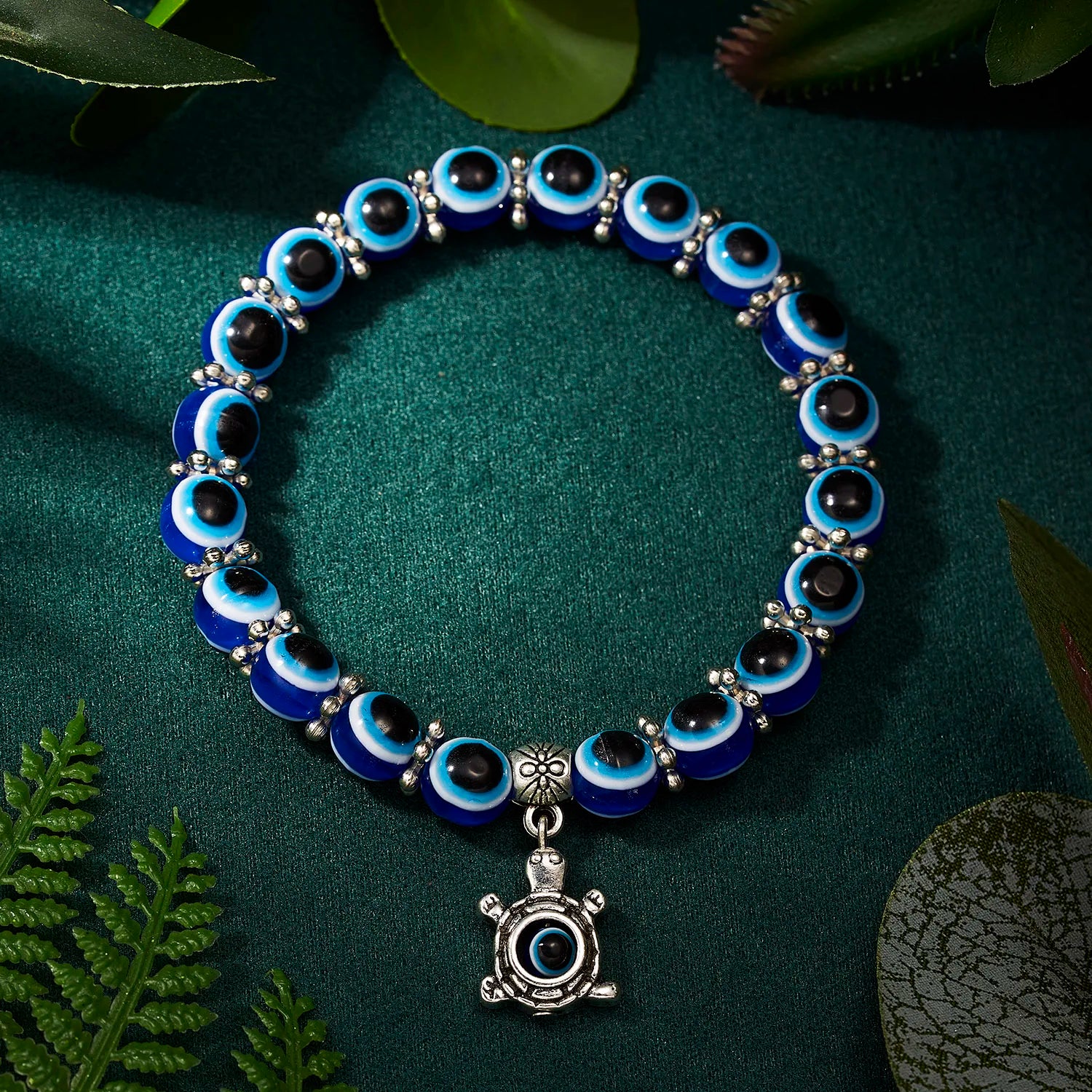 Blue and black beaded bracelet with a silver turtle charm on a green background