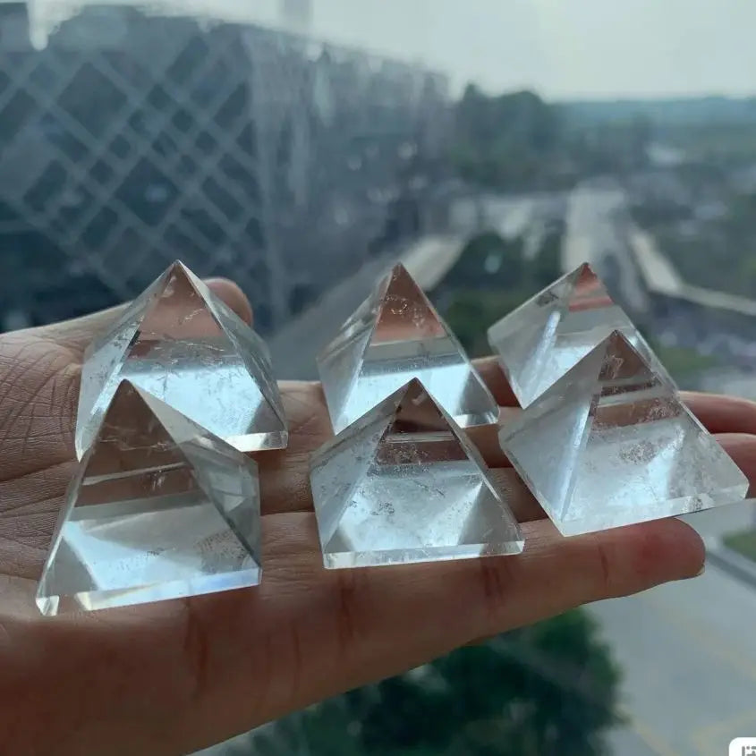 Clear crystal pyramids held in a hand with a blurred outdoor background