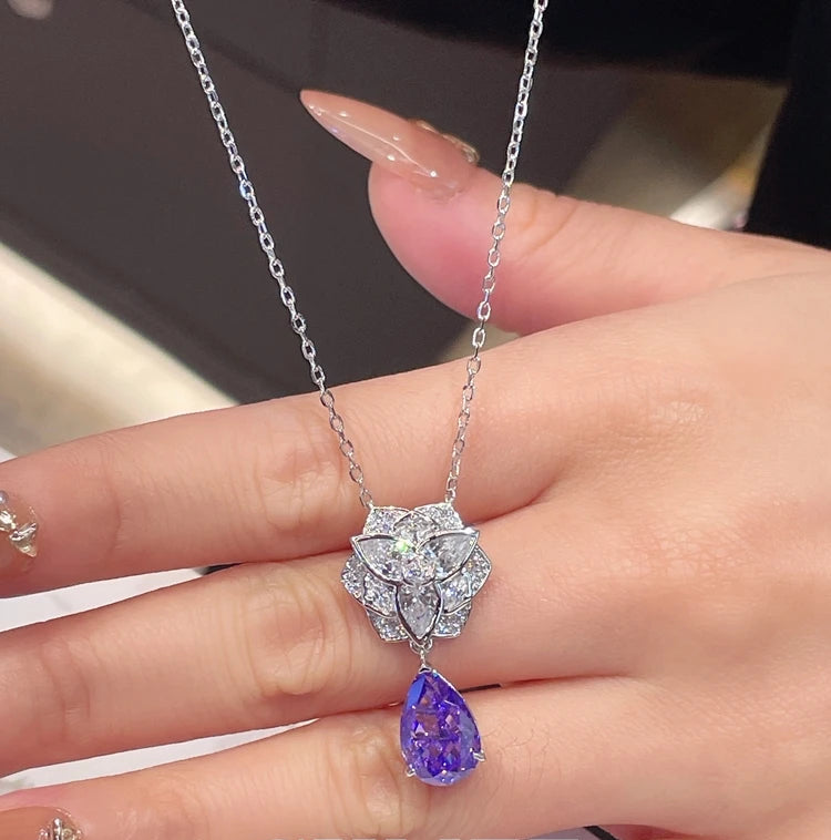 Hand wearing a necklace with a purple pendant, brand 'CUMEE' visible