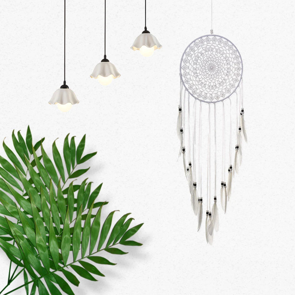 White dreamcatcher with feathers on a white background with green leaves and pendant lights.